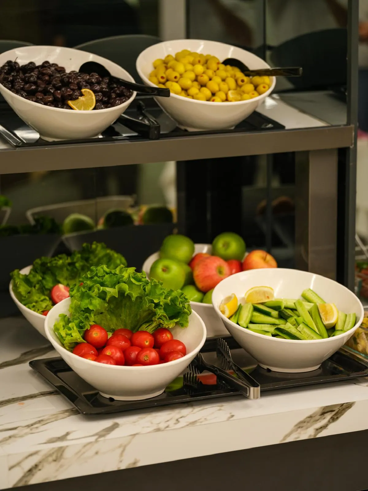 Kahvaltı büfesinde siyah ve yeşil zeytin kâseleri, domates, salatalık ve marul